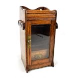An early 20th century oak smoker's cabinet with glazed door enclosing single drawer and racks to