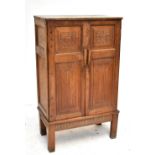 ALAN BROUGH (1890-1986): an adzed oak cabinet, the twin panelled doors with carved foliate and linen
