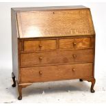 An oak bureau with fall-front enclosing fitted interior above two short and two long drawers on