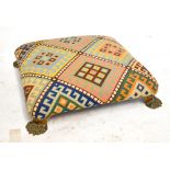 A square foot stool with geometric needlepoint upholstery on four cast brass paw feet, each