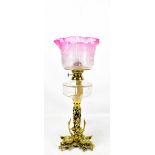 A Victorian brass oil lamp with cranberry glass shade above clear glass reservoir and pierced