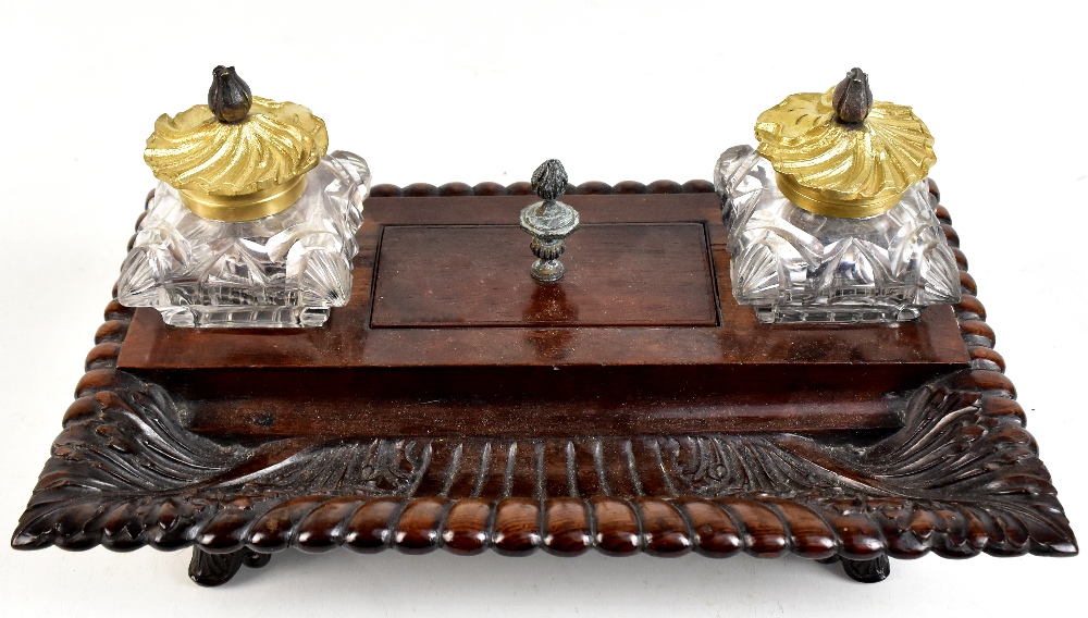 A 19th century rosewood ink standish with twin glass brass mounted inkwells, central lidded