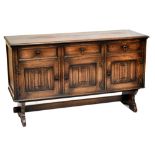 A reproduction oak sideboard with three short drawers above three linen fold detailed cupboard doors