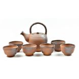 MASANOBU IZUMIHARA; an anagama fired stoneware teapot and six footed bowls, impressed marks,