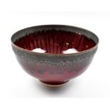 PETER WILLS (born 1955); a porcelain footed bowl covered in copper red glaze with bronze rim,