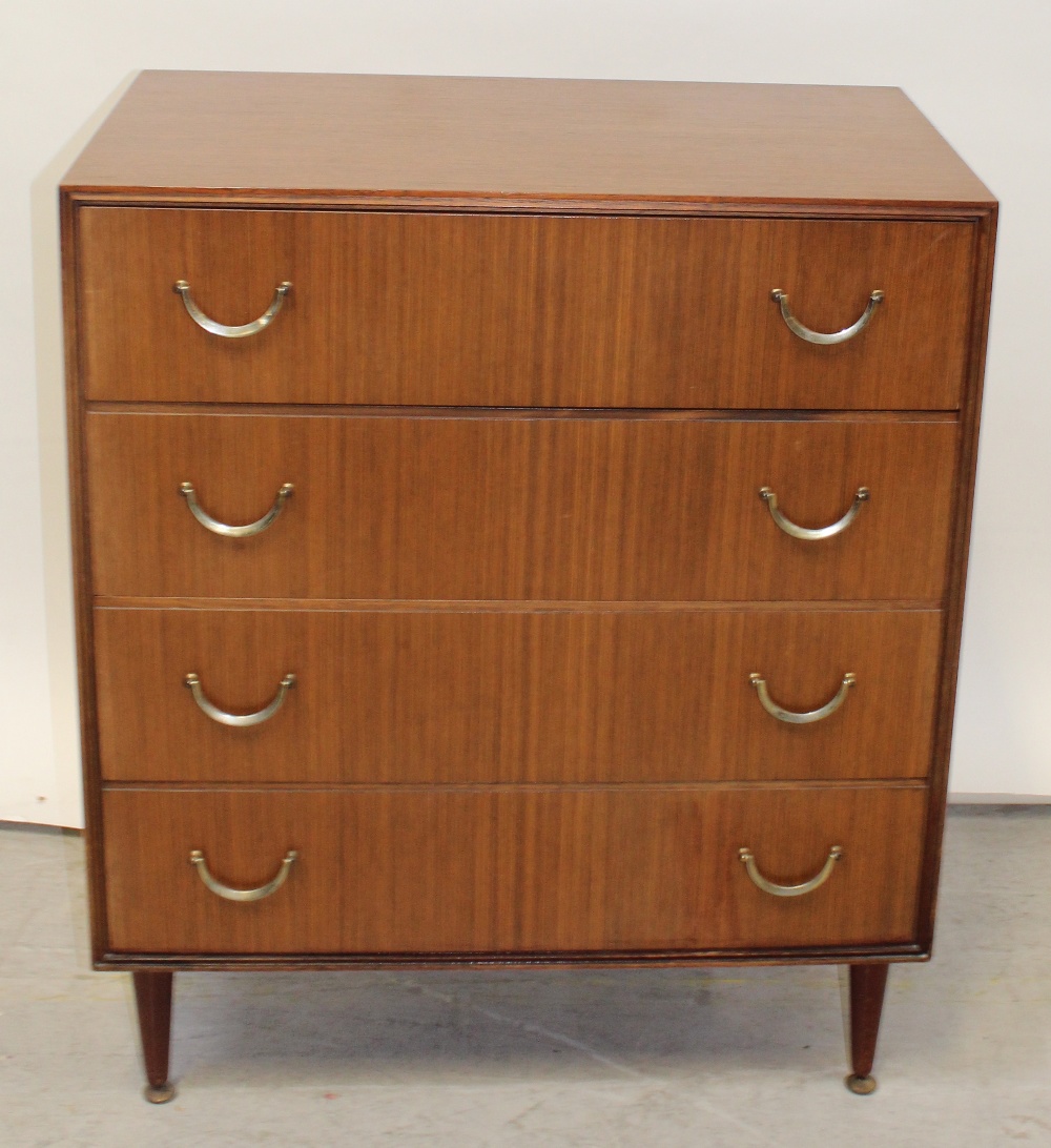 A 1960s teak chest of four long graduated drawers with brass swing handles on tapering legs with