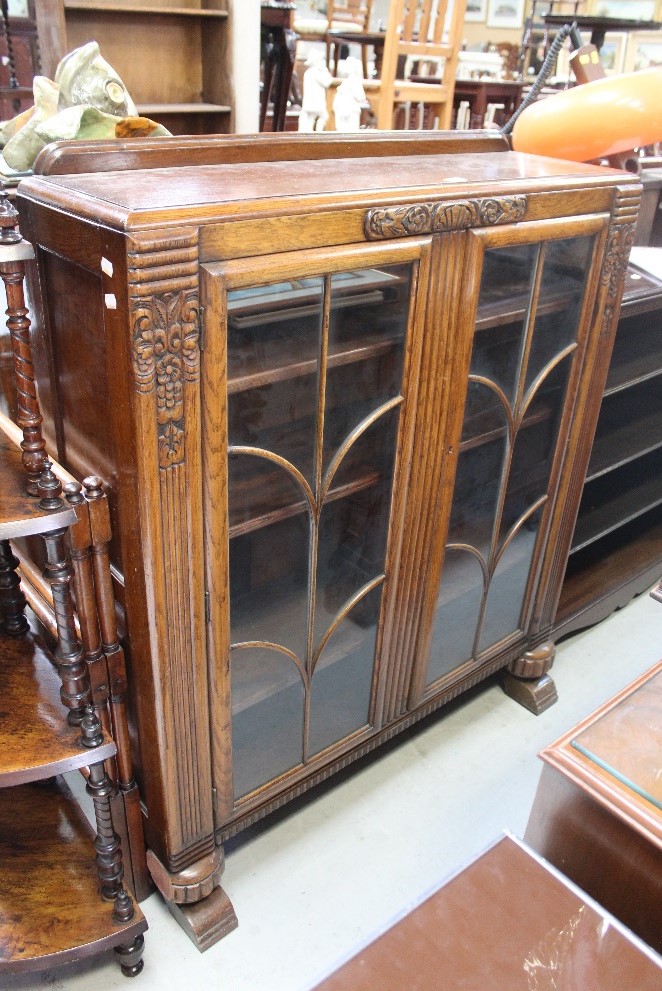 An early 20th century oak display cabinet with carved detail and twin glazed doors enclosing three