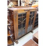 An early 20th century oak display cabinet with carved detail and twin glazed doors enclosing three