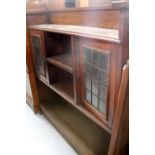 An Arts & Crafts oak bookcase with two leaded glazed doors flanking single shelf and raised on