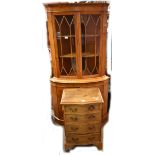 A reproduction yew wood veneered bowfronted free standing corner cabinet with two astragal glazed