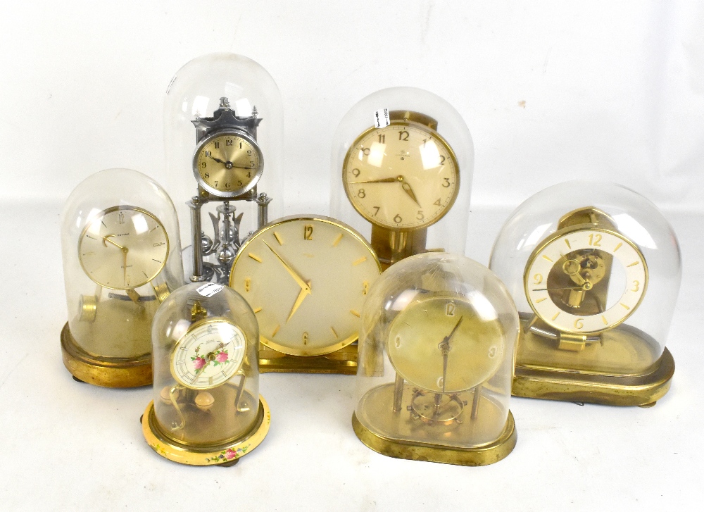 Six anniversary clocks to include a silvered example, each encased in glass and plastic domes, and