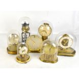 Six anniversary clocks to include a silvered example, each encased in glass and plastic domes, and