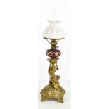 A 19th century oil lamp with opaque white reservoir and cranberry shade on figural column modelled