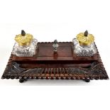 A 19th century rosewood ink standish with twin glass brass mounted inkwells, central lidded