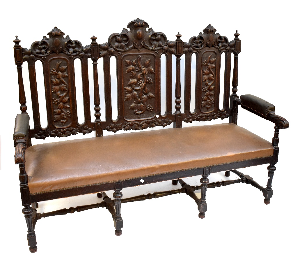 An early 20th century carved oak three seat settee, with foliate detail and light tan upholstery,