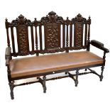 An early 20th century carved oak three seat settee, with foliate detail and light tan upholstery,