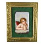 A 20th century hand painted porcelain plaque depicting a cherub, inset in brass frame with Art