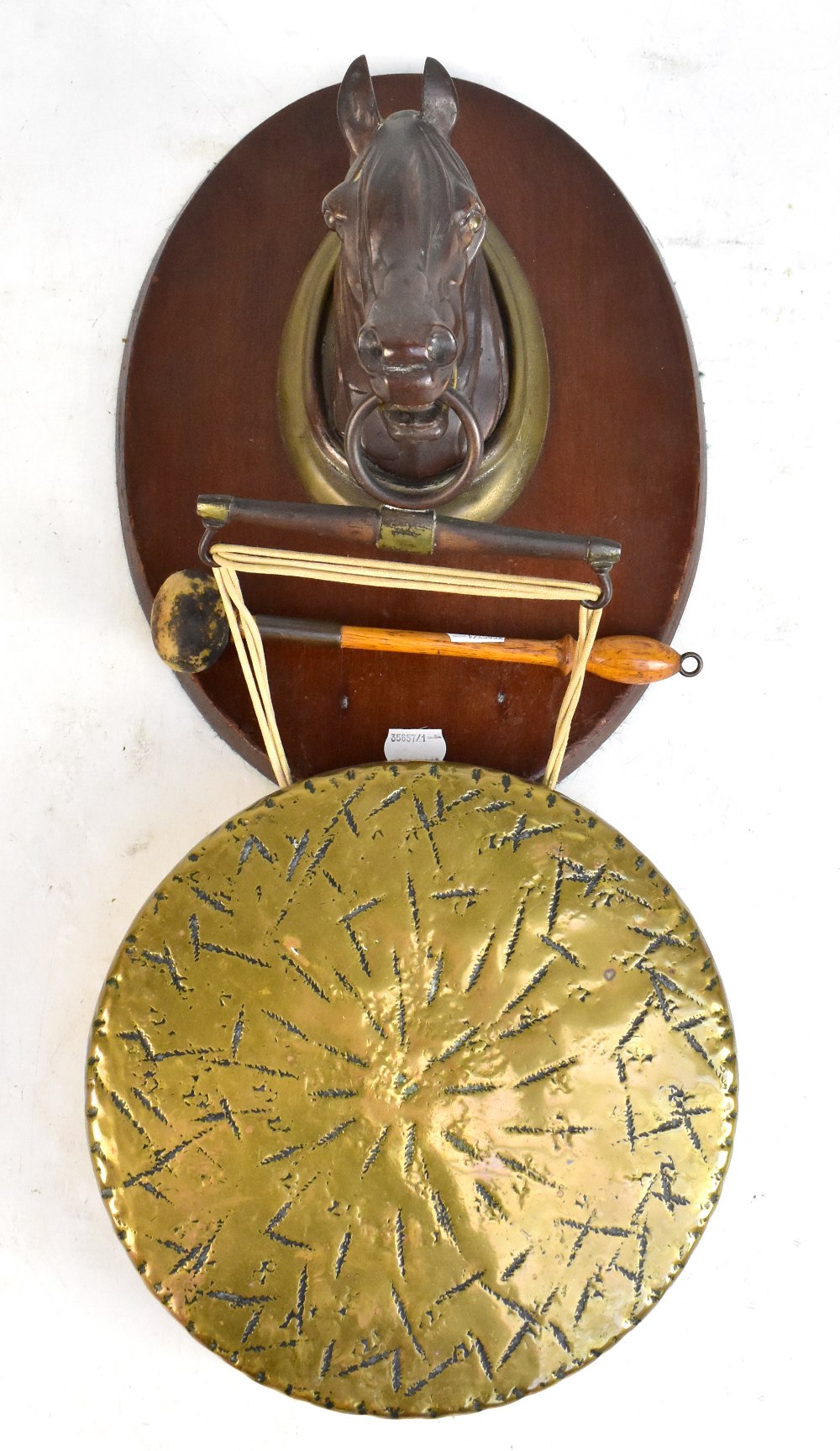 An equestrian themed wall mounted brass gong suspended from a patinated horse's head.