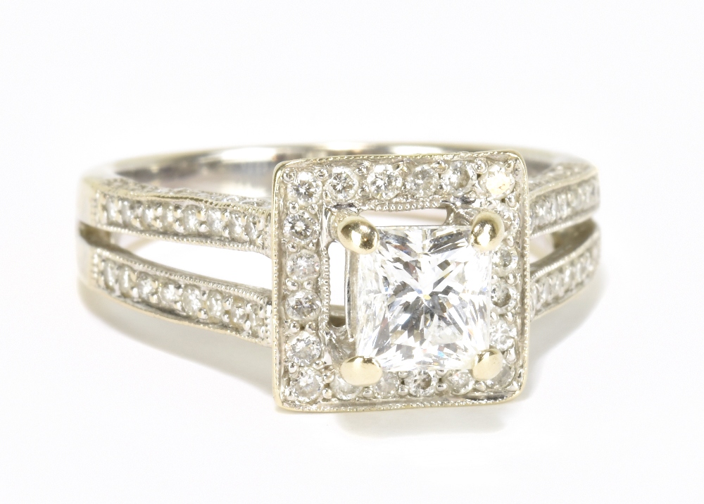 An 18ct white gold and diamond ring, the raised central princess cut stone within a border of twenty