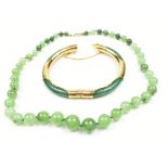 A jade bangle with gold plated mounts, diameter 7.5cm, and a set of graduated beads (2).