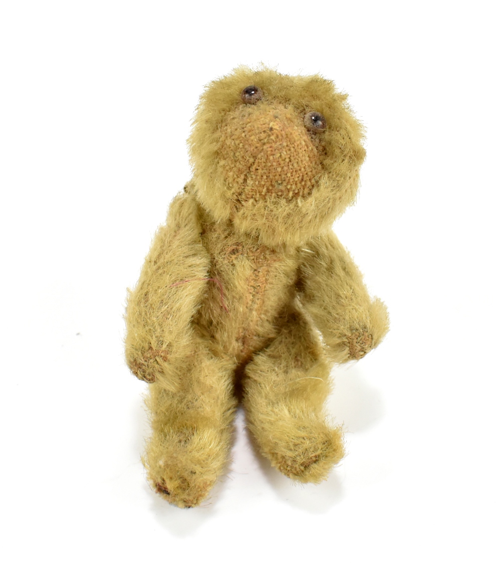 A miniature blonde plush teddy bear with glass eyes and jointed limbs, length approx 9.5cm.