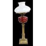 A Victorian brass oil lamp with faceted cranberry glass reservoir and milk glass shade, height