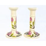 MOORCROFT; a pair of tubeline decorated 'Magnolia' pattern candlesticks on cream grounds, both