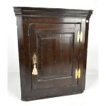 An 18th century dark oak flat fronted hanging corner cupboard with brass H-hinges, height 66cm.