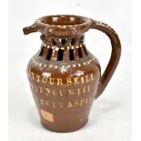 An early 19th century treacle glazed puzzle jug inscribed 'gentlemen now try your skill I'll lay you