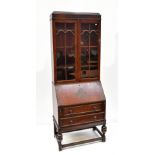 An early 20th century oak bureau bookcase, the twin glazed doors enclosing three shelves, above fall