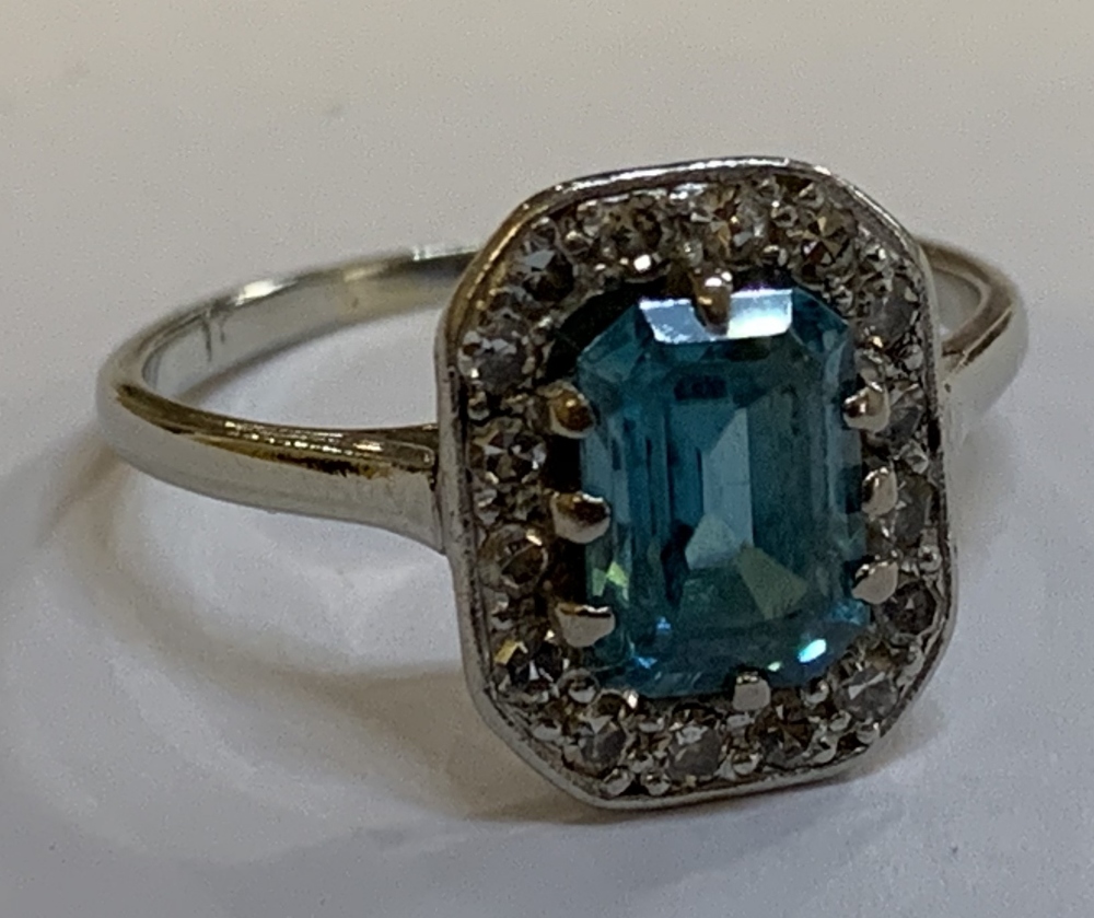 An Art Deco white metal diamond set cocktail ring with central emerald cut stone within a border