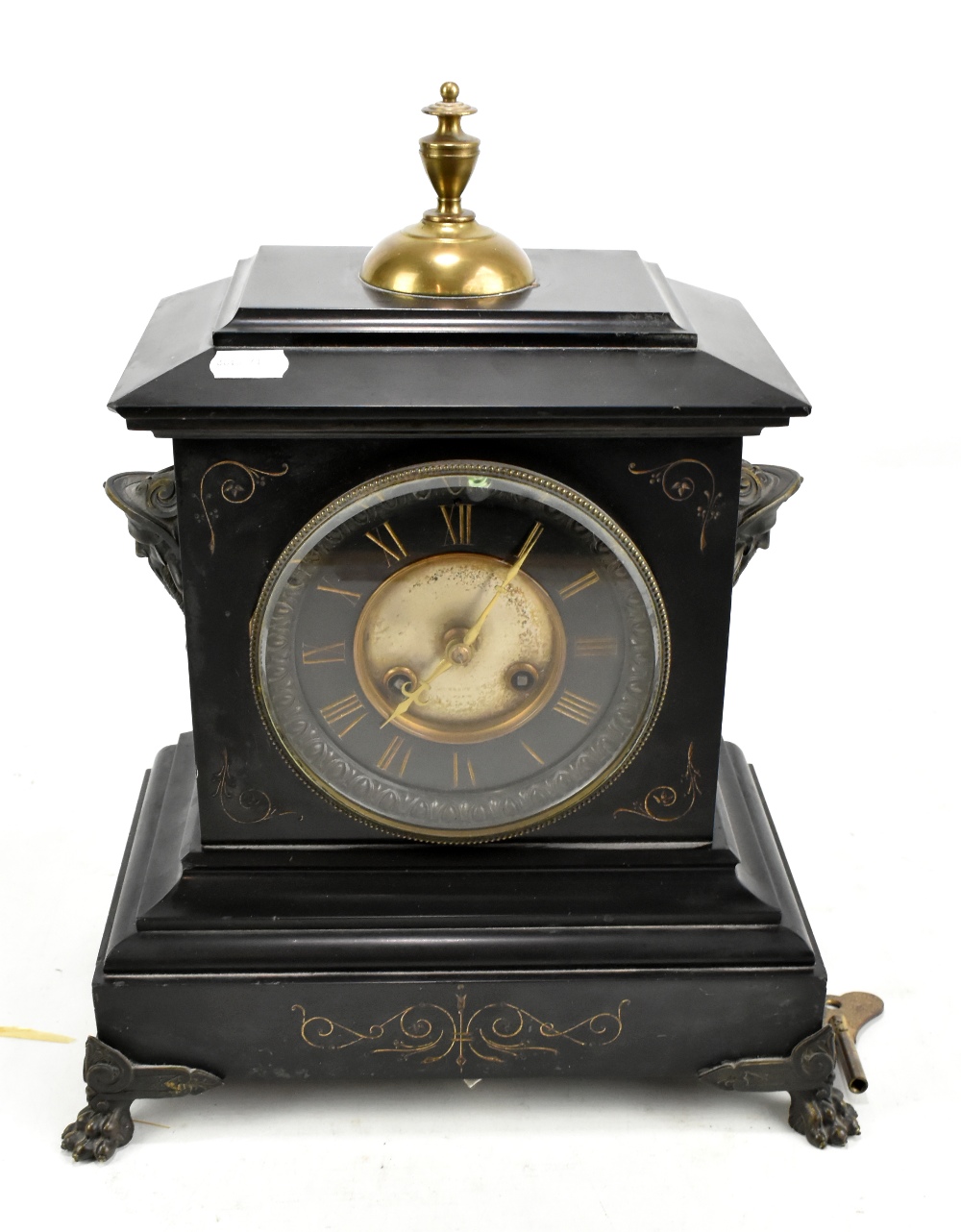 A late 19th century French black slate mantel clock with brass finial and twin masks to either side,