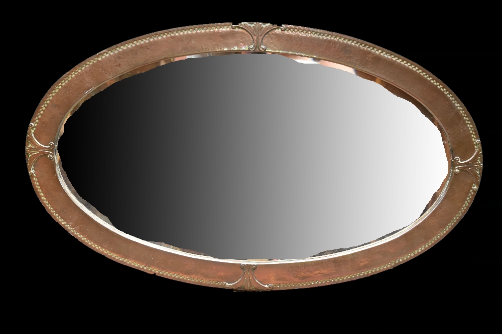 An Arts and Crafts copper framed oval mirror with hammered finish and bevelled glass, 80 x 47cm.