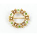 A yellow metal floral wreath brooch set with green coloured stones and cultured fresh water seed