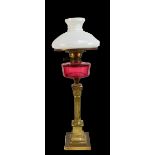 A Victorian brass oil lamp with faceted cranberry glass reservoir and milk glass shade, height 72cm.