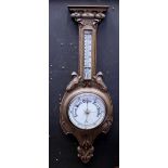 A 1920s barometer/thermometer on carved floral oak mount, height 90cm.