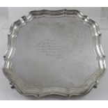 A George V hallmarked silver salver of square form, with piecrust edge, raised on four hoof feet,