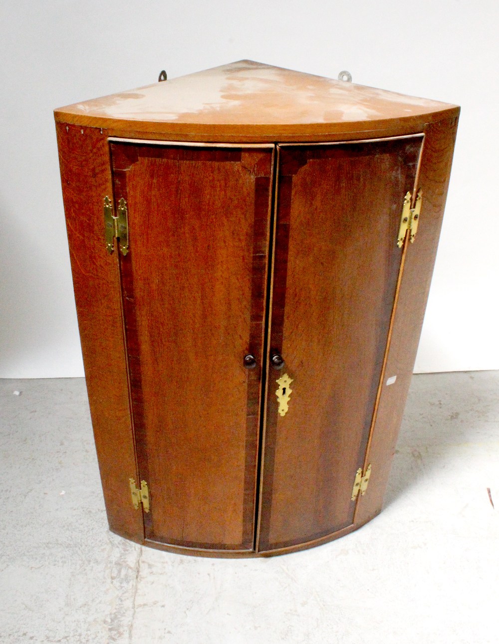 A 19th century cross-banded oak two-door bow-fronted wall-hanging corner cupboard with exposed