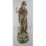 A Royal Dux figure of a young shepherdess standing on a stylised rocky plinth with two kid goats at