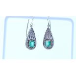 A pair of white metal earrings set with diamonds and emeralds.