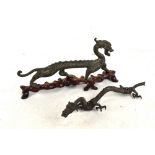 A Chinese cast metal figure of a stylised dragon raised on an associated shaped wooden base,