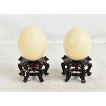 A pair of blown ostrich eggs mounted on Chinese hardwood stands, overall height 23cm, height of eggs