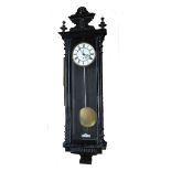 A 19th century ebonised Vienna style wall clock with carved finial of a mask head, above circular