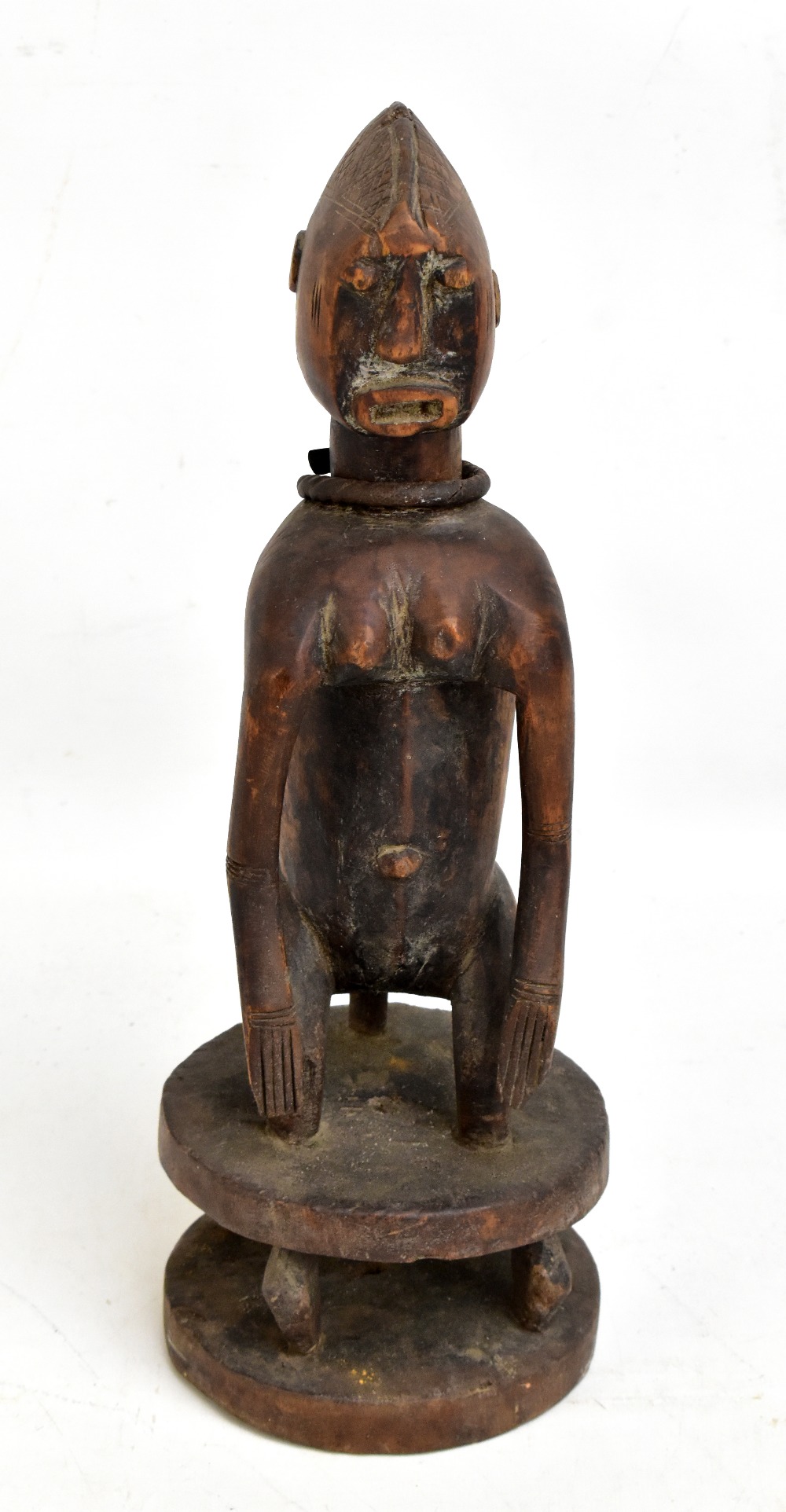 A Chamba figure carved squatting on a circular base, wearing an iron necklace, height 39cm.