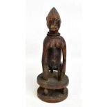 A Chamba figure carved squatting on a circular base, wearing an iron necklace, height 39cm.
