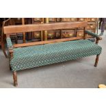 A late 19th/early 20th century oak framed bench with green floral upholstery on turned front