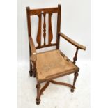 An Arts & Crafts oak framed armchair with carved detail on turned tapered supports with 'X'