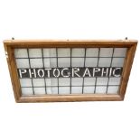 A 20th century leaded stained glass advertising panel 'Photographic' set in pine frame, 60 x 117cm.