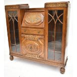 An early 20th century oak side by side bureau bookcase, the central fall front with carved floral