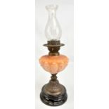 A Victorian oil lamp with peach glass reservoir and foliate detailed foot to circular base (